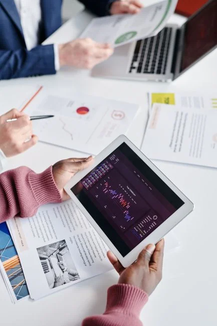 Hands using smartphone trading app with charts, dollar bills in background.